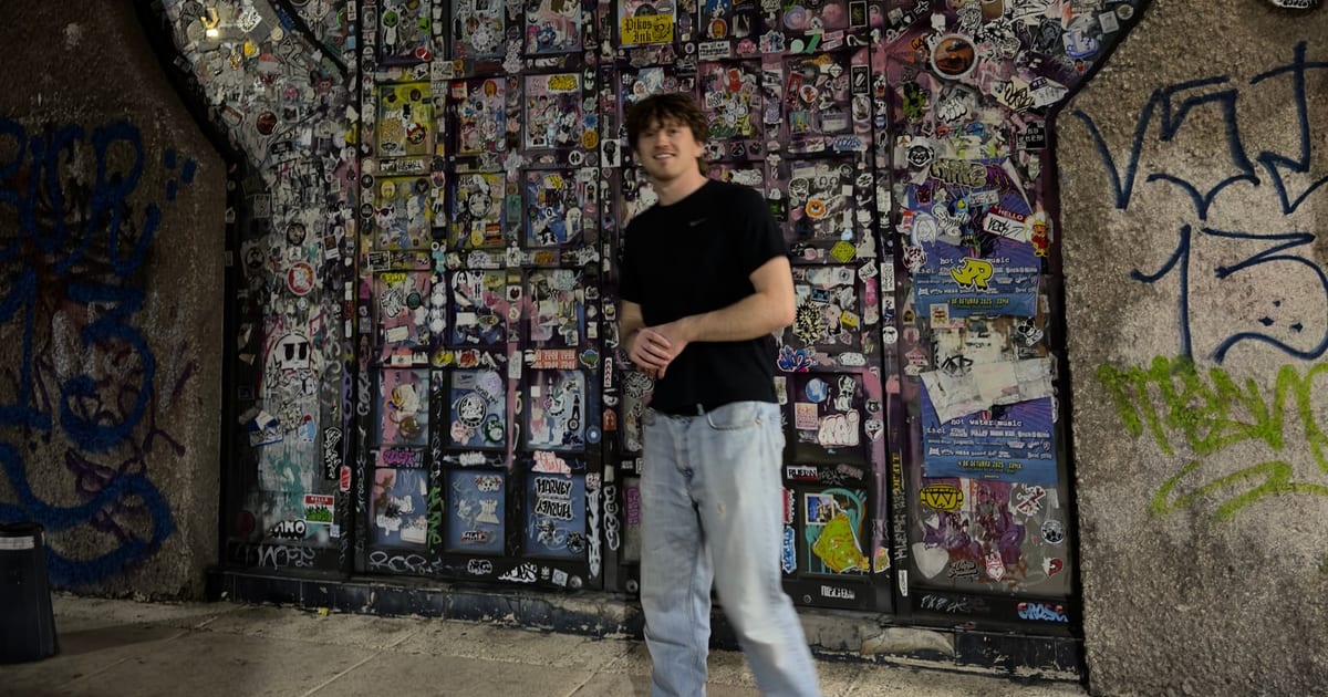 RYLAND in front of a sticker-covered wall at night